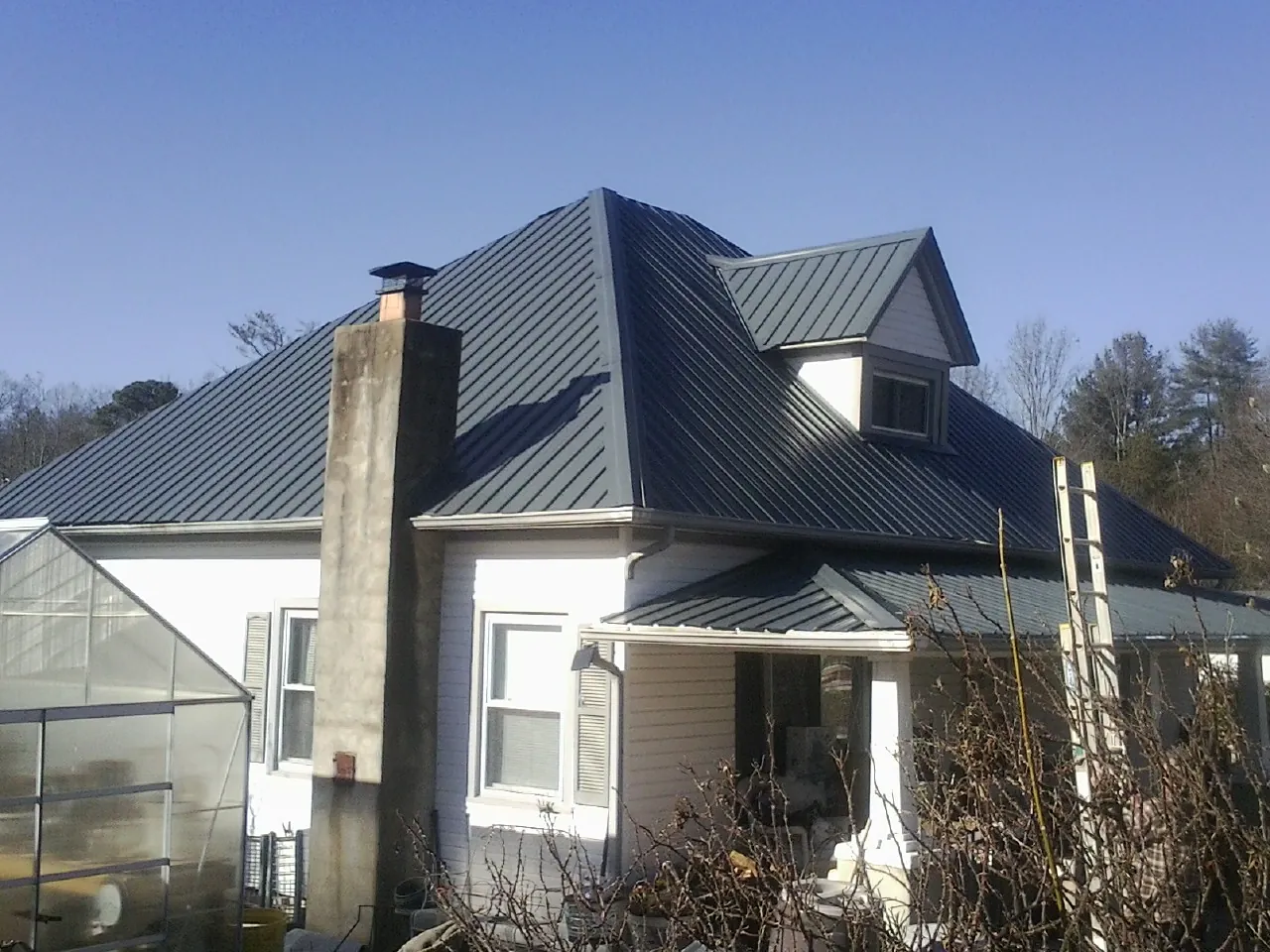 Dark blue standing seam metal roof on a white farmhouse with dormer — Slate & Tile Roof Repair by Roofing Brothers in Glendo