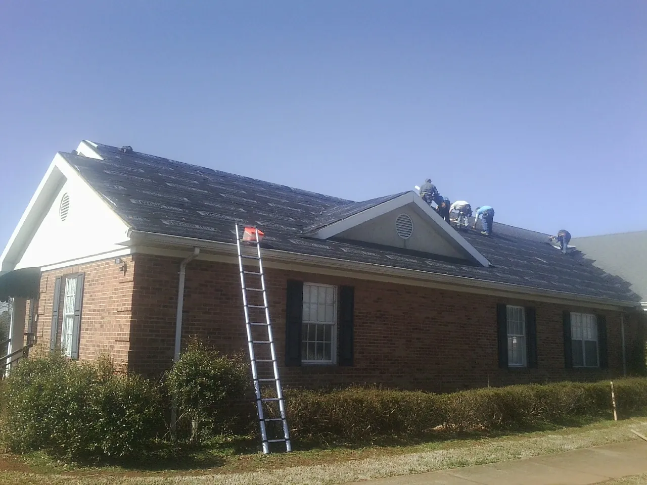 Crew tearing shingles off a brick ranch roof with a ladder set — Emergency Roof Repair work by our crew in Glendo