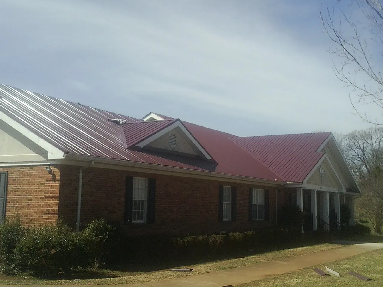 Red metal roof with gabled entries on a long brick building, from a Hail Damage Roof Repair job in Glendo
