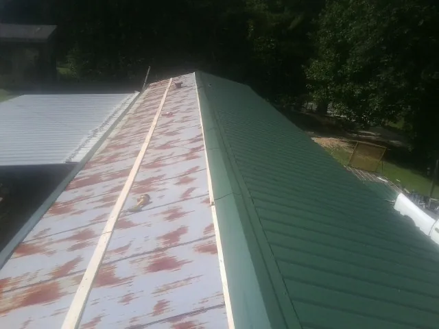 Old rusted panels beside newly installed green metal roofing — Wind Damage Roof Repair by Roofing Brothers in Glendo