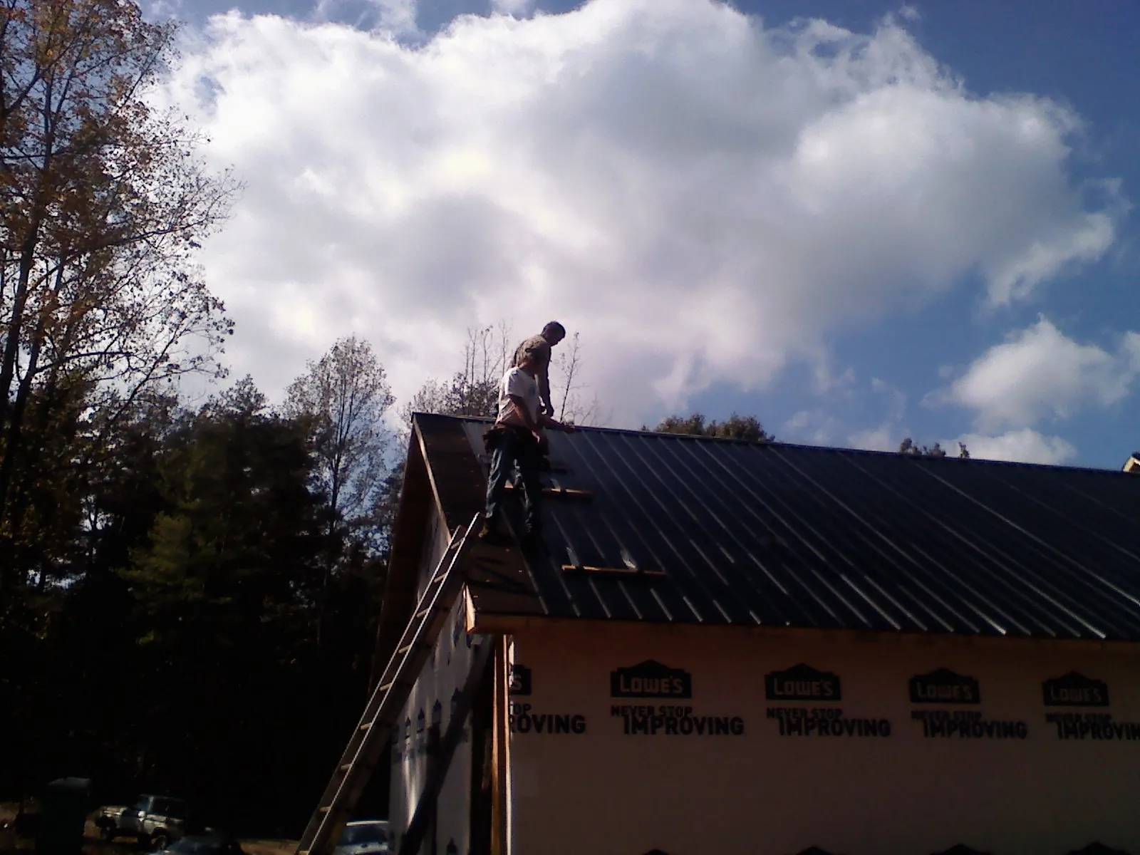 Roofer fastening dark metal panels high against a cloudy sky, from a Roof Inspection job in Glendo