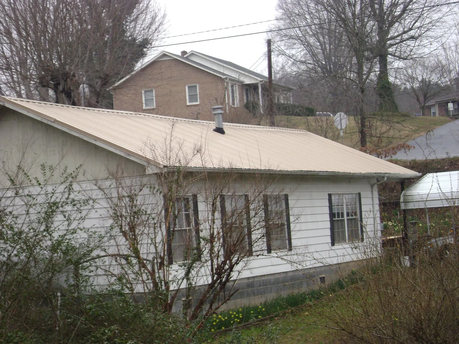 Tan metal roof on a white sided house set into a hillside — Commercial Roofing by Roofing Brothers in Glendo