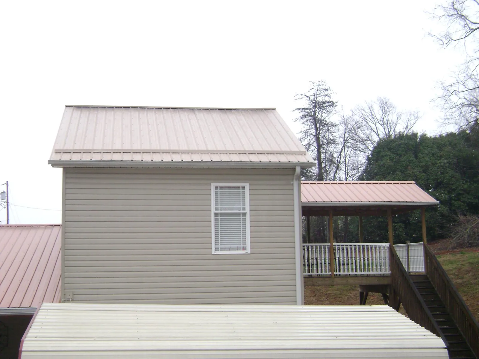 Tan metal roofs on a two story addition and attached porch, from a Roof Replacement job in Glendo